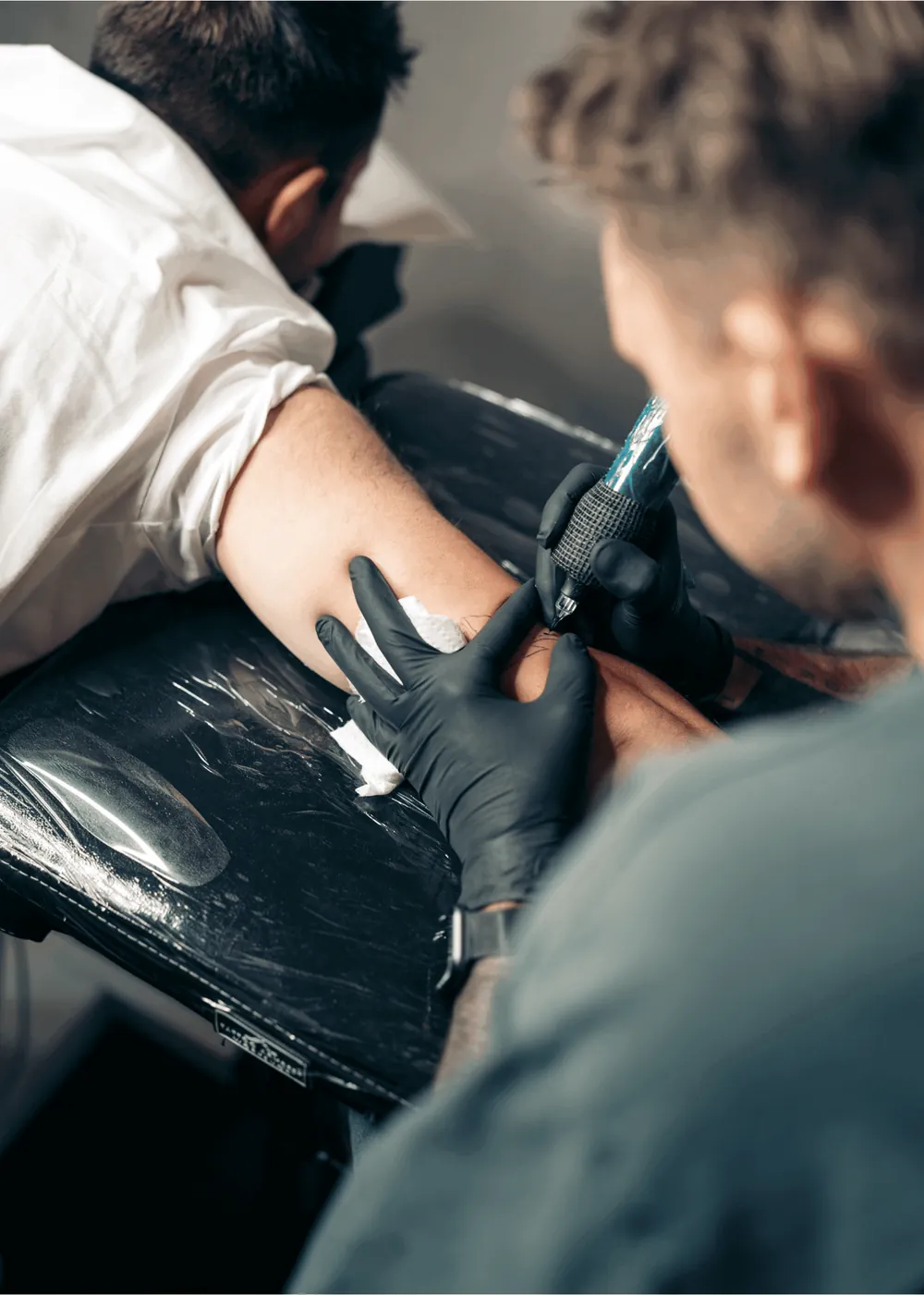 Tätowierer mit schwarzen Handschuhen sticht ein Tattoo am Oberarm