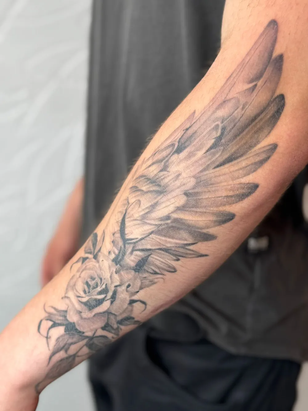 Unterarm-Tattoo mit Flügel und Rose in Schwarz-Grau